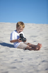 Happy boy sitting on a sandy beach looking at camera - ZEF004892