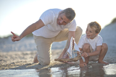 Vater und Sohn spielen mit einem Spielzeugboot in einem Wasserbecken an einem Sandstrand - ZEF004784