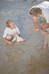 Vater und Sohn spielen mit einem Spielzeugboot in einem Wasserbecken an einem Sandstrand - ZEF004785