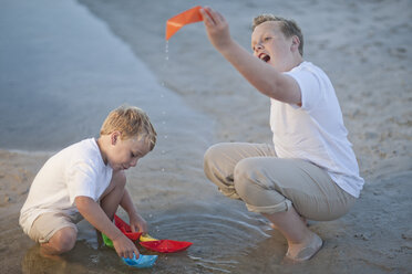 Zwei Jungen spielen mit Papierbooten in einem Wasserbecken an einem Sandstrand - ZEF004787