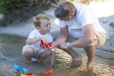 Vater und Sohn spielen mit Papierbooten in einem Wasserbecken an einem Sandstrand - ZEF004789