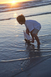 Junge spielt mit einem Spielzeug-Holzboot im Wasser an einem Strand - ZEF004796