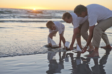 Vater und Söhne spielen mit Spielzeug-Holzbooten im Wasser an einem Strand - ZEF004895
