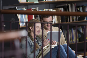 Zwei Studenten sitzen in der Bibliothek und schauen auf ein digitales Tablet - ZEF004349