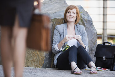 Businesswoman taking a break, sitting on ground rolling cigarette - ZEF003861