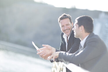 Businessmen leaning at railing, talking - ZEF003883