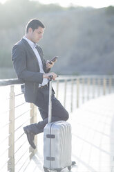 Busnessman with suitcase looking at mobile phone - ZEF003884