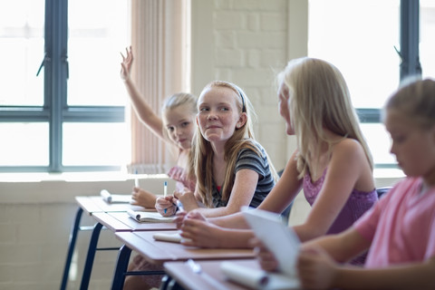 Schulmädchen im Klassenzimmer hebt ihre Hand, lizenzfreies Stockfoto