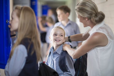 Teacher helping schoolgirl with backpack on hallway - ZEF004959