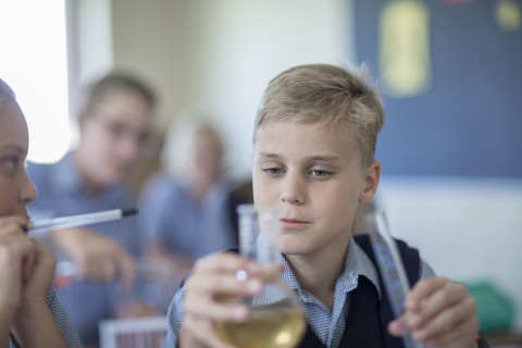 Schülerin im Chemieunterricht mit Blick auf einen Rundkolben, lizenzfreies Stockfoto