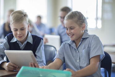 Two smiling pupils in classroom sharing digital tablet - ZEF004978