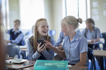 Zwei glückliche Schulmädchen im Klassenzimmer mit Mobiltelefon - ZEF004980