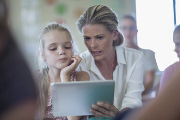 Teacher with digital tablet talking to schoolgirl in classroom - ZEF004991