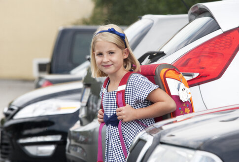 Portrait of little girl with school bag between parking cars - WWF003626