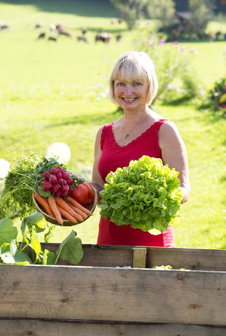 Österreich, Mondsee, Porträt einer lächelnden Frau mit ihrer Gemüseernte, lizenzfreies Stockfoto