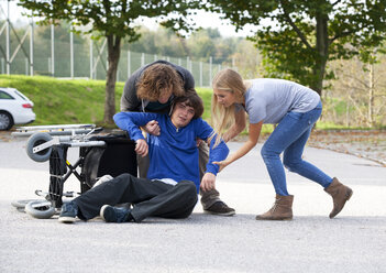 Zwei junge Leute helfen einem jungen Rollstuhlfahrer nach einem Sturz - WWF003650