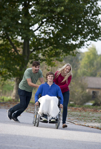 Junges Paar mit Freund im Rollstuhl sitzend, lizenzfreies Stockfoto