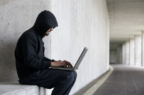 Hacker with laptop sitting in an underground car park - WWF003642