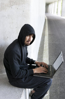 Porträt eines Hackers mit Laptop, der in einer Tiefgarage sitzt - WWF003667
