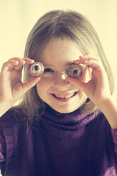 Lächelndes kleines Mädchen, das sich zwei Litschis vor die Augen hält - SARF001293