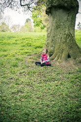 Kleines Mädchen sitzt vor einem alten Baum auf einer Wiese - SARF001294