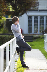 Austria, Mondsee, smiling young woman leaning against railing telephoning with smartphone - WWF003894