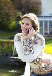 Austria, Mondsee, portrait of smiling young woman leaning on railing telephoning with smartphone - WWF003895