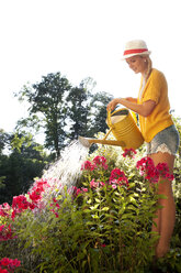 Junge Frau gießt Blumen im Garten - WWF003678