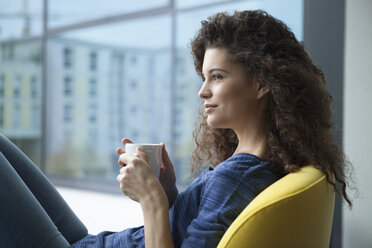 Junge Frau mit Tasse Kaffee schaut aus dem Fenster - RBF002311