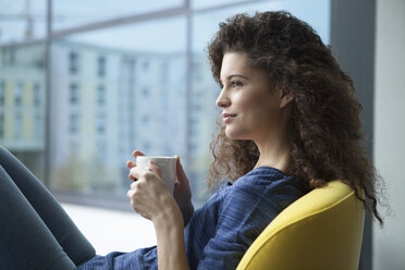 Young woman with cup of coffee looking out of window - RBF002311