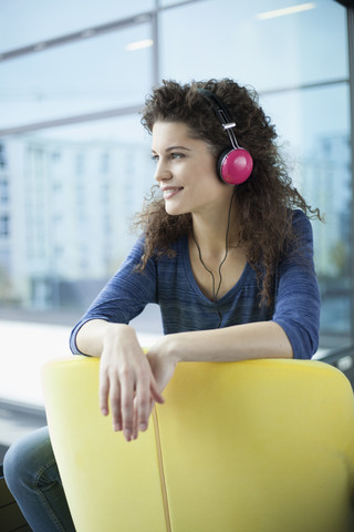 Lächelnde junge Frau mit Kopfhörern am Fenster, lizenzfreies Stockfoto