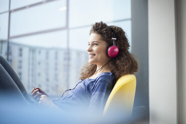 Smiling young woman wearing headphones at the window - RBF002323