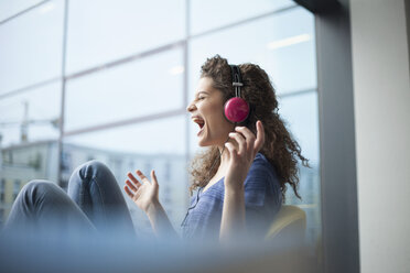 Screaming young woman wearing headphones at the window - RBF002324