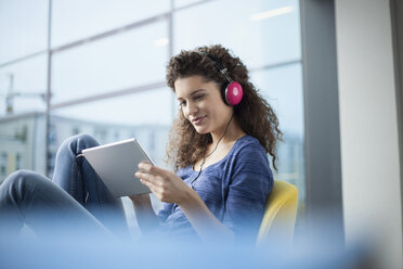 Lächelnde junge Frau mit Kopfhörern und digitalem Tablet am Fenster - RBF002325