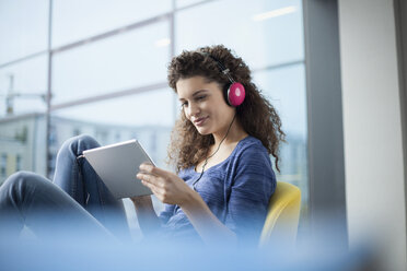 Smiling young woman wearing headphones and using digital tablet at the window - RBF002325