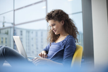 Smiling young woman using laptop at the window - RBF002327
