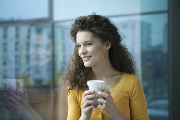 Lächelnde junge Frau mit einer Tasse Kaffee am Fenster - RBF002333