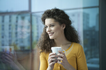 Smiling young woman with cup of coffee at the window - RBF002333