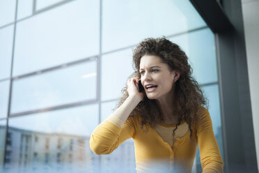 Wütende junge Frau am Telefon am Fenster - RBF002339