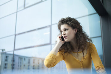 Verängstigte junge Frau beim Telefonieren am Fenster - RBF002340