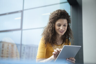 Lächelnde junge Frau mit digitalem Tablet am Fenster - RBF002341