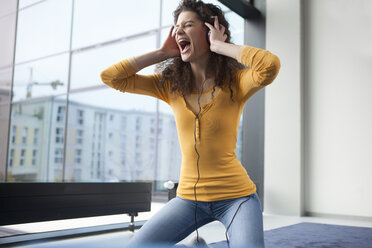 Screaming young woman wearing headphones at the window - RBF002342