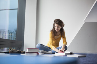 Studentin sitzt mit Büchern auf dem Boden - RBF002345