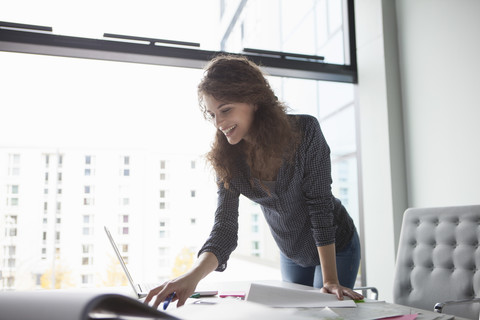 Junge Frau mit Laptop am Schreibtisch im Büro, lizenzfreies Stockfoto