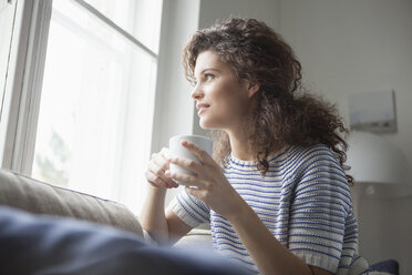 Smiling young woman with cup of coffee looking out of window - RBF002362