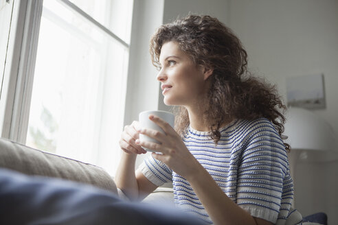Lächelnde junge Frau mit einer Tasse Kaffee und Blick aus dem Fenster - RBF002362