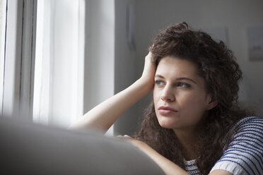 Junge Frau zu Hause mit Blick aus dem Fenster - RBF002286