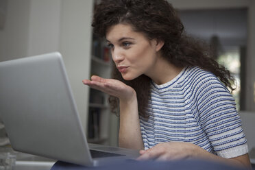 Junge Frau zu Hause am Laptop bläst einen Kuss - RBF002307