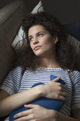 Serious young woman lying on sofa with hot water bottle - RBF002289