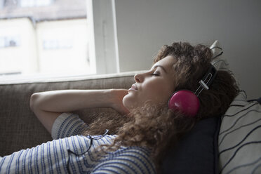 Young woman lying on couch wearing headphones - RBF002263